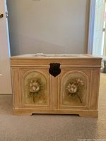 Front view of the wooden decorative storage chest with painted flowers on two panels and a metal latch.