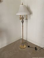 Full view of floor lamp showing metal and glass body, white fabric lampshade, power cord with step-on switch.