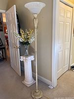 Full view of floor lamp standing about 70 inches tall next to wall and pedestal with flowers.