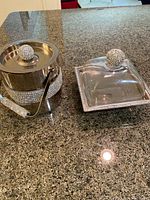 Photo showing silver ice bucket with rhinestone band and lid, alongside a matching serving tray with glass cover and rhinestone knob on granite countertop