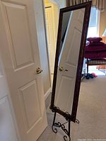 Full view of the full-length mirror standing upright, showing the wooden frame and wrought iron stand with curled feet.