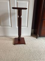 Full view of the solid wood multi-purpose stand with square top, carved vertical column, and square base.