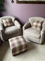 Pair of beige upholstery armchairs with plaid cushion and plaid ottoman in front.