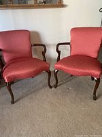 Pair of upholstered duck chairs with reddish-pink fabric and dark solid wood frames on carpeted floor.