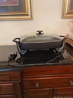 Black rectangular Presto electric skillet with glass lid, power cord attached, sitting on a wooden surface.
