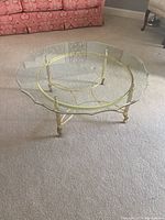 Full side view of the round coffee table showing clear scalloped glass top and polished brass base with ornate feet.