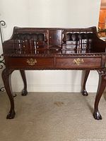 Front view showing multiple small drawers, two large drawers with brass handles, carved legs and detailed edges
