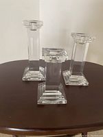 Front view of three glass candleholders of different heights on dark wood surface.