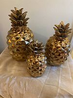 Front view of three gold decorative pineapples of varying sizes placed on a soft cloth surface