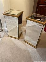Pair of mirrored pedestals with gold trim shown from an angle to display reflective surfaces and general condition.