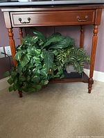 Front view of the solid wood table showing drawer and lower shelf with plants.