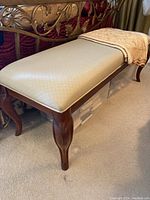 Full view of bench showing upholstered beige seat and carved wooden legs.