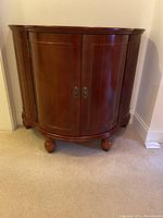 Front view of the closed dark wood curved wine cabinet resting on bun feet.