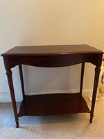 Front view of a wooden table with a shelf showing its shape and leg details.