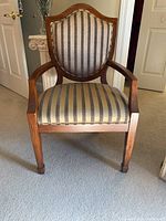 Front view of wooden chair showing striped upholstered seat and shield-shaped upholstered backrest with wooden arms and legs.
