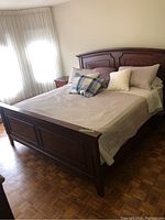 King size bed with beige quilted linens, pillows, dark faux wood paneled headboard and footboard.