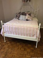 Full view of white painted metal bed with pink bedding, set against parquet wood floor.