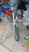 Photo showing white Nakamura bicycle with blue fork and black tires in garage alongside scooter and other items.