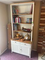 Full view of two-piece laminated book shelf with contents on shelves and cabinet below, showing white finish and wood-toned top surface on cabinet.