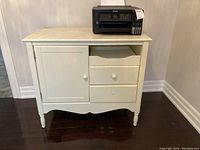 Front view of white melamine cabinet showing two drawers and one door, one drawer knob missing.