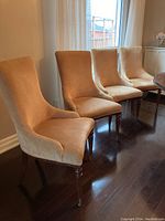 Four chairs arranged in a row next to a window on dark hardwood flooring