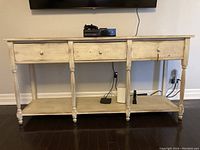 Front view of wood console table with three drawers and lower shelves on dark floor.