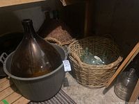 Two large demijohns and basket of smaller glass bottles placed on rustic wooden floor, basement setting