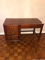 Front view of a wood desk with three drawers on the left side and noticeable wear to the finish.
