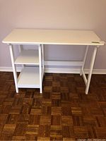 Front view of white painted desk showing two lower shelves on left side and angled legs on right side.