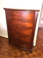 Front view of tall faux wood dresser with five curved drawers and locks.