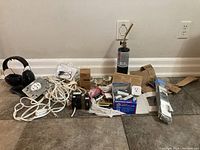 Photo showing a variety of electrical supplies and accessories including outlets, switches, extension cords, ear protection, and a torch placed on the floor.