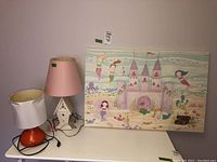Two lamps and canvas art on white table against pale pink wall, front view