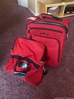 Roots red soft-sided duffel bag with shoulder strap, zipper opened to show interior space and logo.