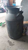 Front view of metal milk can showing cylindrical shape with two side handles and rust spots.