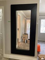 Front view of the large rectangular mirror with thick black wood frame hanging on a wall.