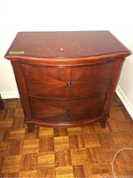 Front view of a single faux wood nightstand showing two drawers with lock-style handles and visible wear on top surface.