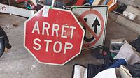 Photo showing the two metal road signs leaning against other items in a garage, including a Canadian style stop sign and a no U-turn sign showing rust.