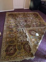 Full view of the rectangular Indo-Kashan patterned rug laid flat on a purple carpet with one corner lifted to show the underside and fringes.