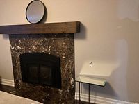 Overall view of room corner showing side table positioned next to fireplace and round mirror hung above the fireplace mantel.