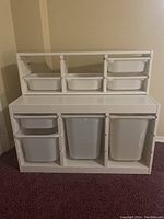 Front view of both large and small white painted wood storage bins cabinets showing arrangement and size of plastic bins.