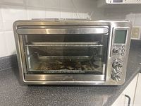 Front view of the Hamilton Beach toaster oven showing the large glass door, metal handle, and digital control panel with knobs.