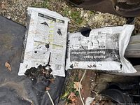 Photo shows two white plastic bags labeled Asphalt Repair, both have multiple holes and appear damaged, showing signs of outdoor storage and use.