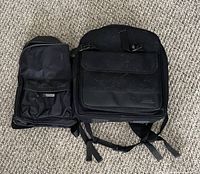 Two black backpack-style bags placed on carpet, showing front view with pockets and straps visible