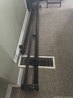 Metal side rails of bed frame with wheel casters and adjustable support brackets laid out on carpeted floor.
