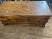 Front view of wooden cedar chest with metal latch and hinges visible.