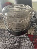 Full view of the electric food dehydrator showing six stacked transparent circular trays on a black base with a clear domed lid.