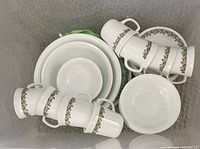 Stack of white ceramic cups with green leaf pattern, white bowls, and serving plates.