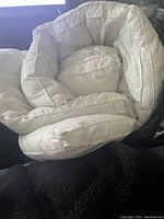 Rolled up white duvet on a dark surface, showing thickness and quilting details.