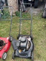 Black deck gas lawn mower with visible engine and wheels, shown outdoors on grass.