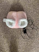 Pink heated slippers with white fleece lining, placed on carpet, showing front and opening for feet.